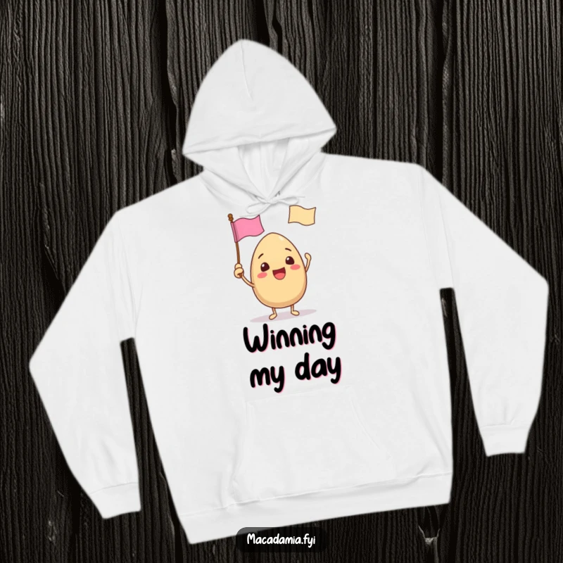 Funny hoodie with a macadamia nut character excitedly waving a tiny flag with a funny face, offering cozy celebration.
